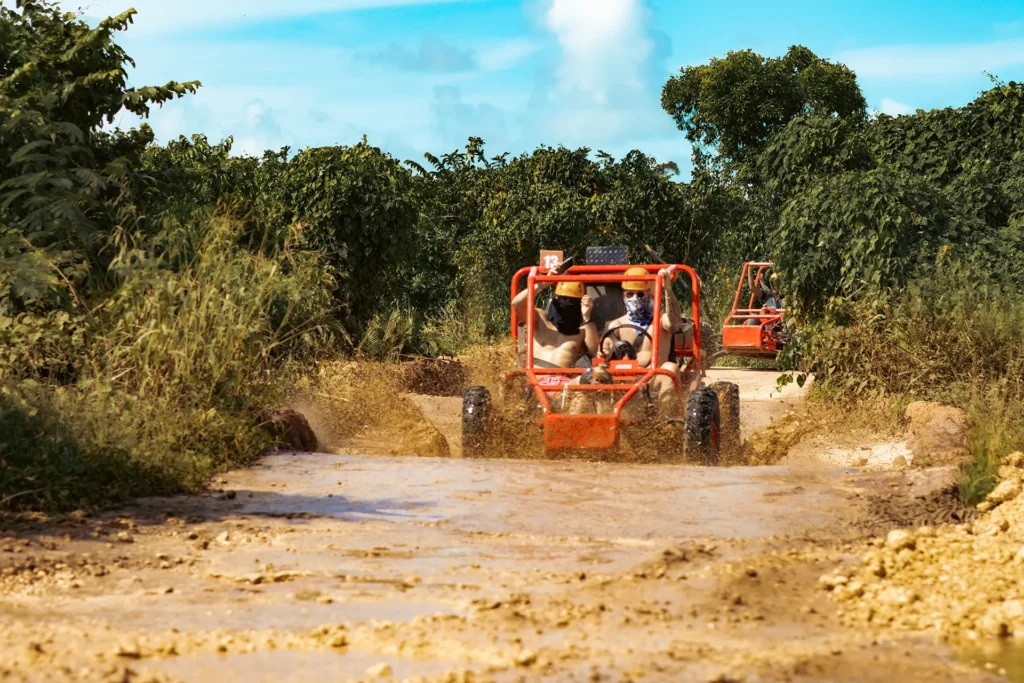 Línea de buggies rojos avanzando por un camino rural embarrado rodeado de vegetación tropical durante el tour.