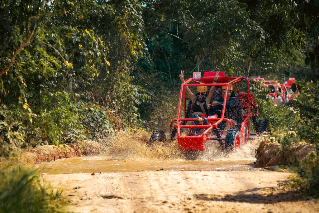 Turistas sonrientes conduciendo un buggy 4x4 rojo a través de un charco de lodo en una pista todoterreno en Punta Cana.